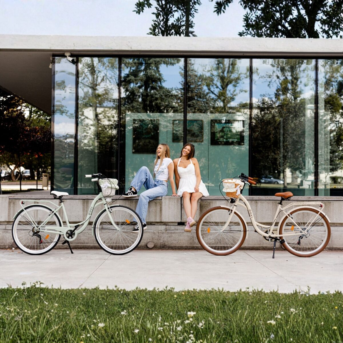 Två kvinnor sitter utomhus nära två cyklar.