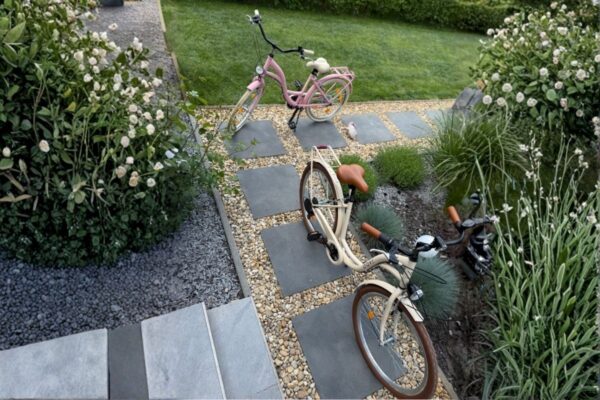 Två cyklar i trädgård med grus och stenstig.