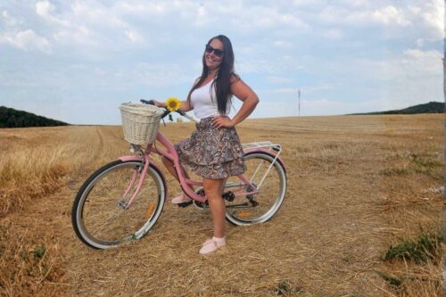 Kvinna med rosa cykel på sommarfält.