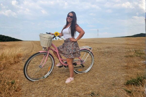 Kvinna med rosa cykel på sommarfält.