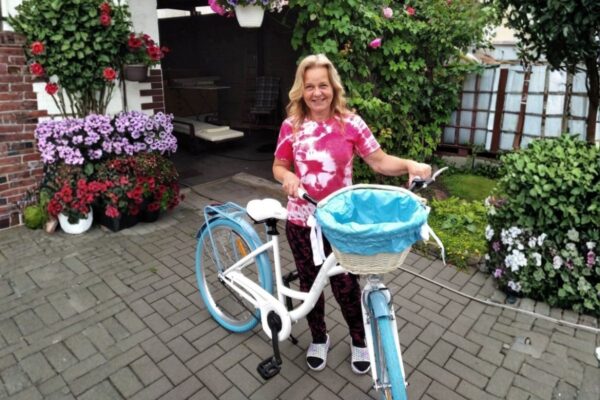 Kvinna med cykel framför blommande trädgård